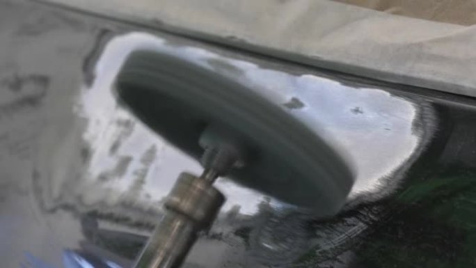 一名男子在汽车车身上使用圆形砂光机的细节照片