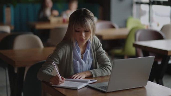 年轻美丽微笑的亚洲女商人拿着咖啡和笔记本电脑放在办公室的木桌上。妇女在远程办公时检查邮件或进行研究
