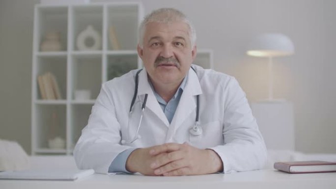 中年男医生在诊所办公室向网络研讨会或视频会议的参与者打招呼，并讲话，肖像