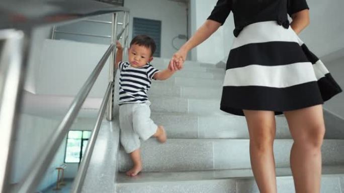 母亲握着蹒跚学步的男孩的手，在楼梯上行走