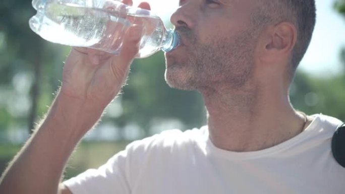 无法识别的高加索成年运动员在阳光照射下在户外喝水并呼吸。疲惫但快乐的白人男子在夏日晨练后休息。