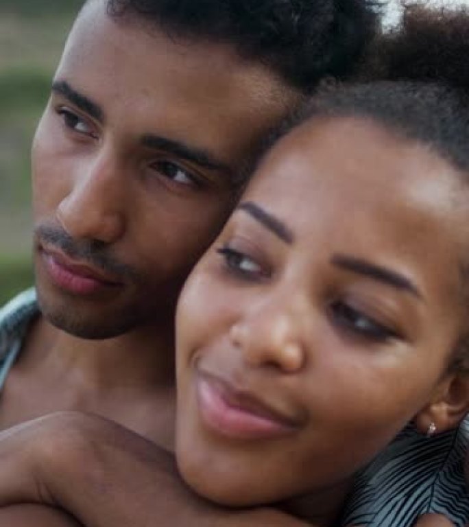 热爱非洲种族的夫妇坐在沙滩上，互相抱着。海滩上的浪漫约会垂直视频