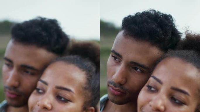 热爱非洲种族的夫妇坐在沙滩上，互相抱着。海滩上的浪漫约会垂直视频