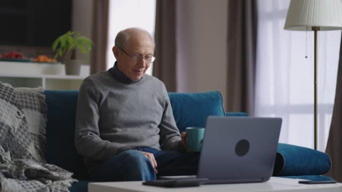 祖父独自一人坐在家里，通过与朋友或家人的视频聊天进行交流，看着笔记本电脑的网络摄像头