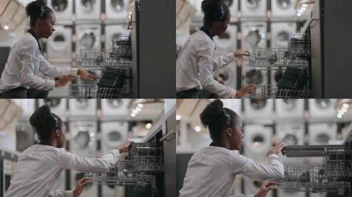 年轻的黑人妇女正在检查家用电器商店洗碗机的内部填充，单身女士正在五金店购物