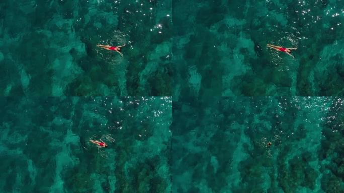 空中无人机拍摄了一名在绿松石水中游泳的妇女