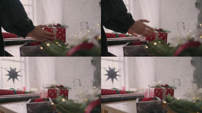 一名年轻女子用花环在木桌上装饰礼物，翻过来，放在桌子上，一个用丝带压碎的现成的圣诞盒子。