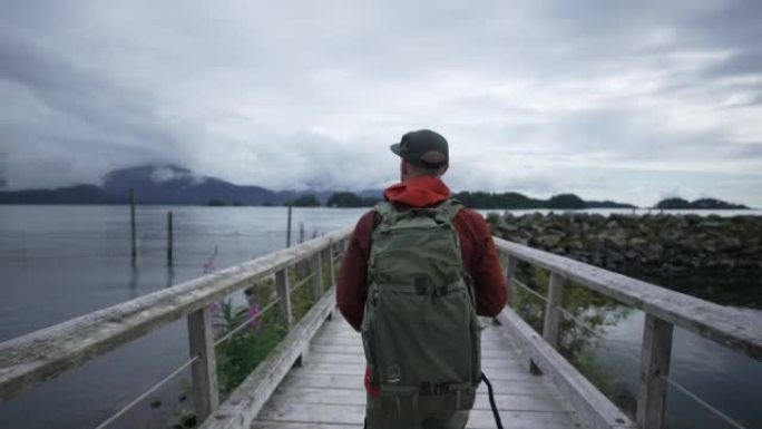 一位年轻的男摄影师在山区海湾附近的木桥上的近距离拍摄