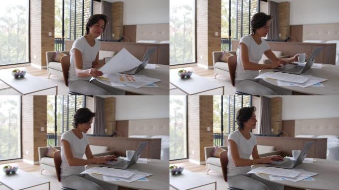 拉丁美洲成熟女性在家工作，新型冠状病毒肺炎在卧室里用文书工作和笔记本电脑一边喝咖啡