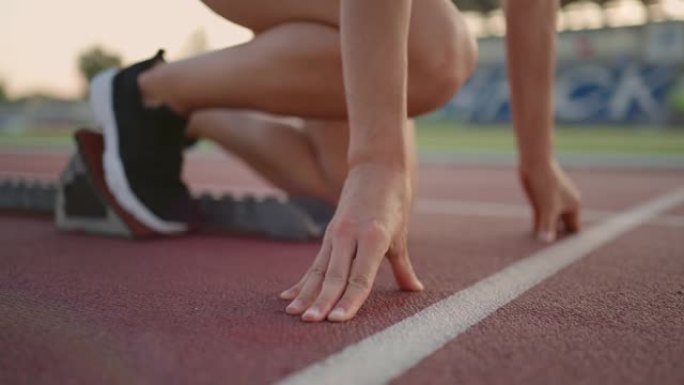 在体育场竞技场的阳光下，一名年轻的女子跑步者为跑步做准备，穿上跑鞋，以慢动作从起跑线冲刺。