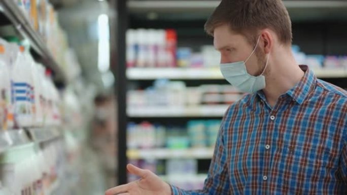 一位戴着口罩的年轻人在超市挑选牛奶和冷冻食品