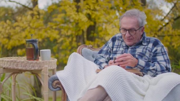 生病的老人病人在外面的椅子上使用手机