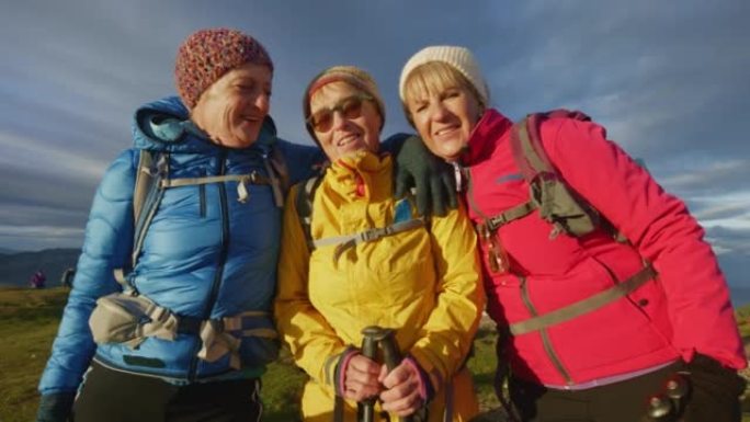 SLO MO三名高级妇女在阳光下徒步到山顶后拥抱并摆姿势