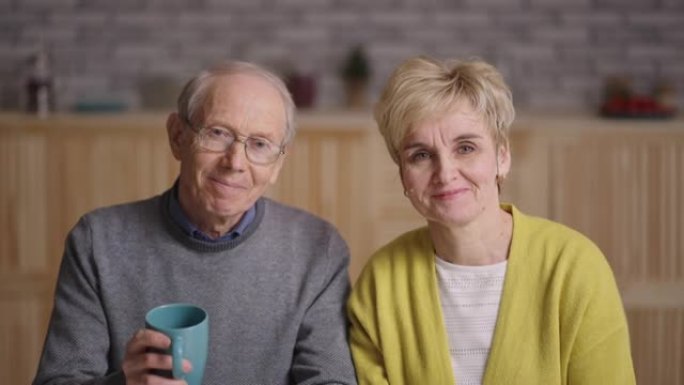 快乐的奶奶和爷爷挥舞着手，看着相机，与家人在线视频聊天，公寓里的厨房