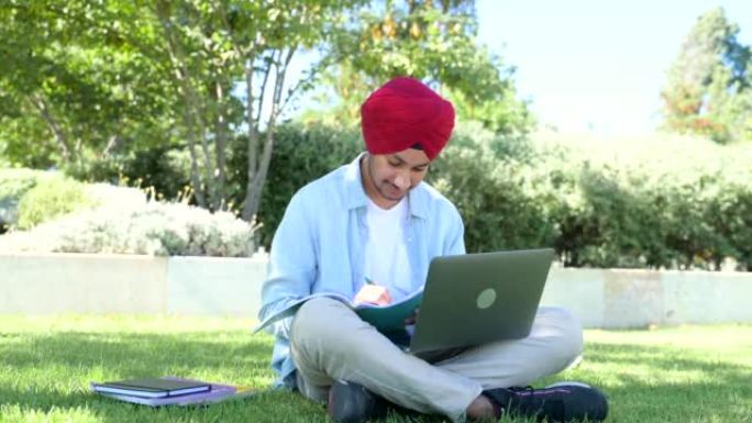 聪明灵感的印度男学生戴着红色传统头套，使用笔记本电脑