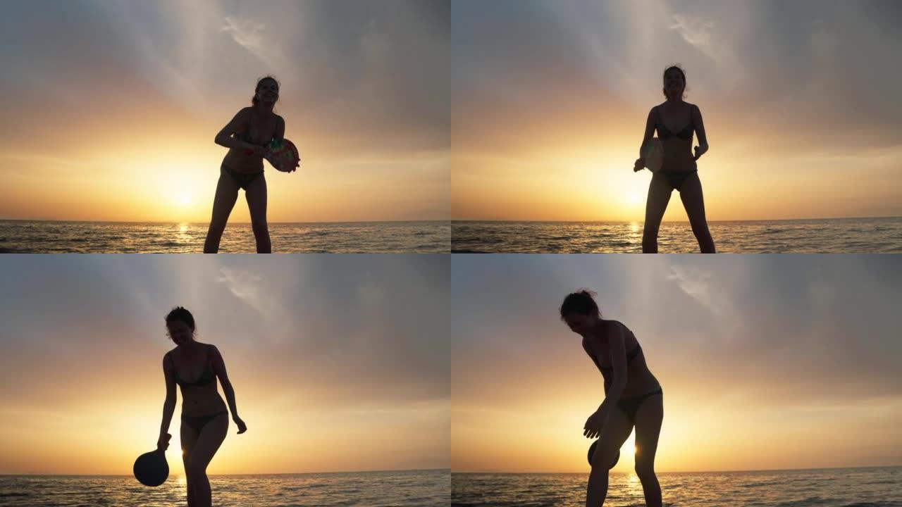 日落时在海滩上享受桨网球的女人的剪影。独自练习