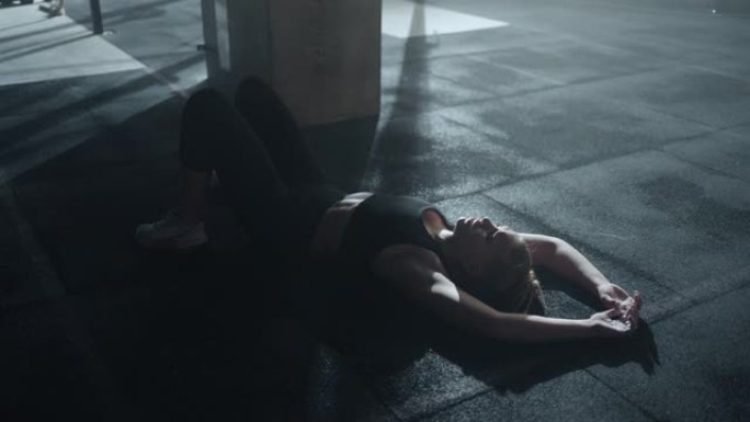 疲惫的女人躺在健身中心的地板上，呼吸困难，在激烈的锻炼后哭泣