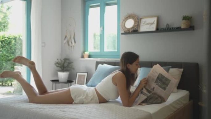 年轻女子躺在床上阅读杂志