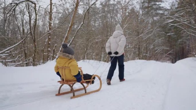 女人正在拉木制雪橇，里面有小孩，冬天在森林里散步