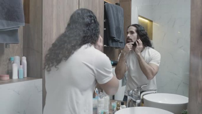自我吸收的男人在胡须上涂抹保湿油，在镜子里欣赏自己