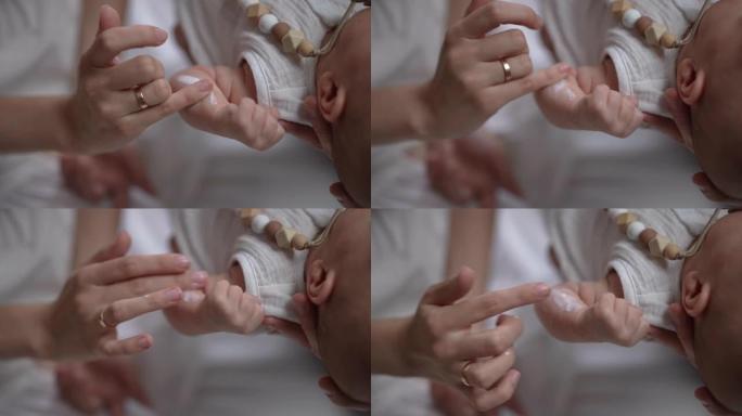 近距离女性手指摩擦保湿霜在新生儿的手在慢动作。无法辨认的高加索母亲在家照顾婴儿儿子。育儿和爱的概念。