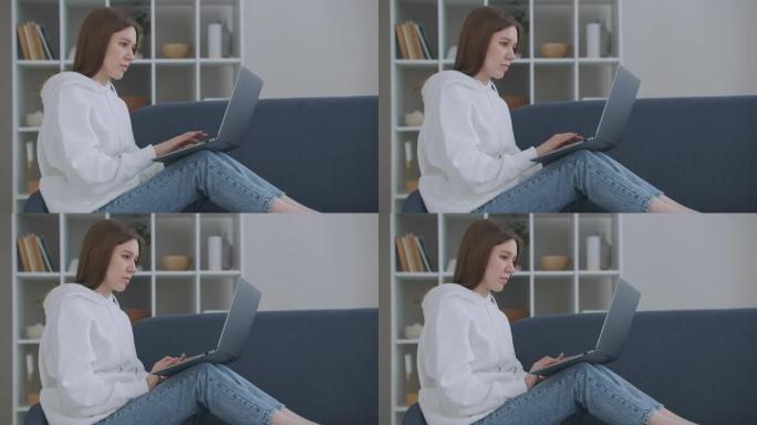 在家沙发上用笔记本电脑的女人。体贴的年轻女子坐在沙发上电脑，看外面，集中精力工作，感到无聊，需要额外