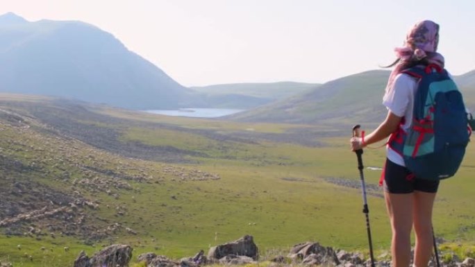 后视图适合运动的女性徒步旅行者，用北欧步行棒站在高加索山脉绿色徒步旅行道上的视点上坡。娱乐活动与健康