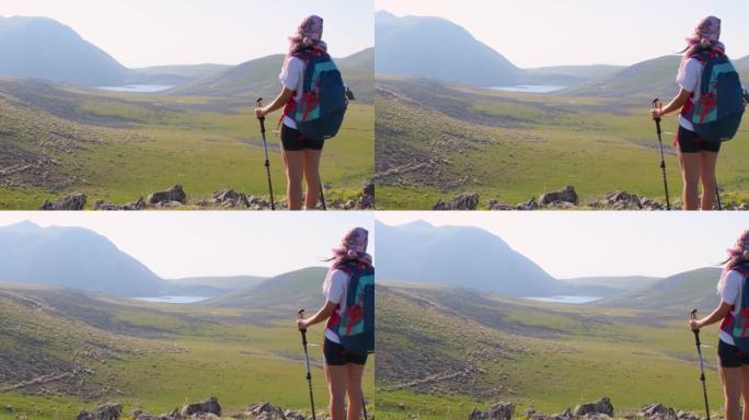 后视图适合运动的女性徒步旅行者，用北欧步行棒站在高加索山脉绿色徒步旅行道上的视点上坡。娱乐活动与健康