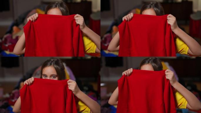 可爱的有趣的少女躲在红色毛衣上看着相机。相当放松的无忧无虑的高加索黑发少年的肖像，棕色的眼睛在室内摆