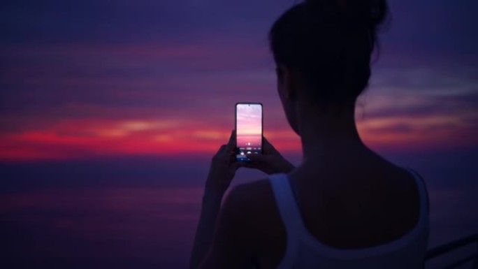 露台上浪漫的日落。女人用智能手机拍照