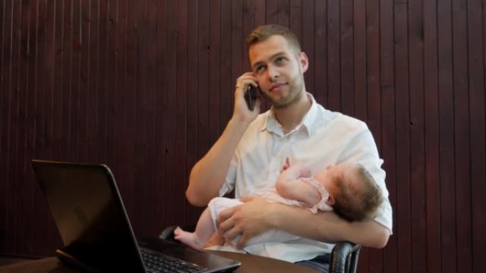 年轻的父亲男子试图在笔记本电脑上工作，并与手机客户端交谈，同时手握着熟睡的女儿孩子