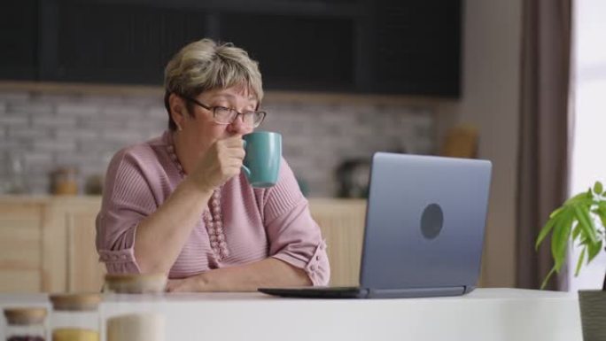 老年妇女白天在家里的厨房里使用笔记本电脑，老太太在网上冲浪的肖像
