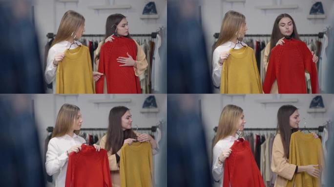 两个年轻漂亮的女人在黑色星期五的商店里选择红色和黄色的毛衣，改变衣架，欣赏镜子里的反射。积极的白人购