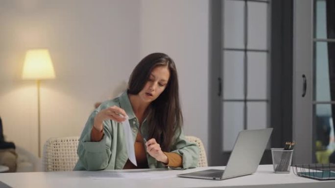 一名女商人在笔记本电脑上远程工作，并在家庭在后台唱歌时在网络摄像头上显示图表。忙碌的女商人。父亲和孩