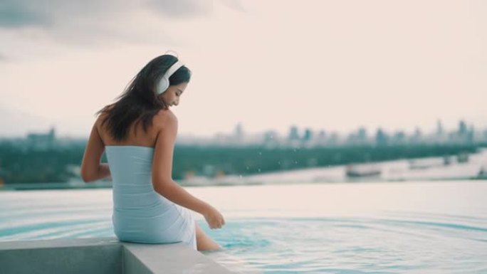 后视图: 亚洲女性戴着耳机听音乐，在池畔愉快地放松