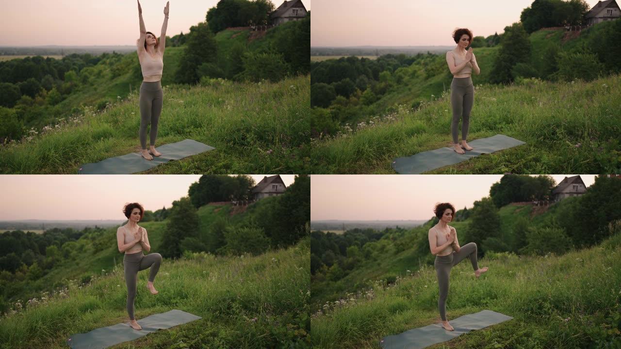 慢动作: 穿着运动服的年轻女子在山上练习瑜伽姿势。摄像机移动创建。女人在户外练习瑜伽。做瑜伽练习的女