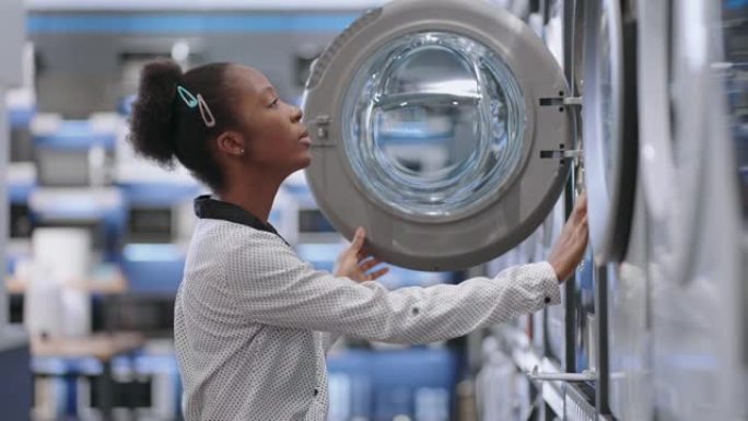 女性购物者正在查看洗衣机，选择新的洗衣设备，在交易大厅拍摄非洲裔美国女性的中型肖像
