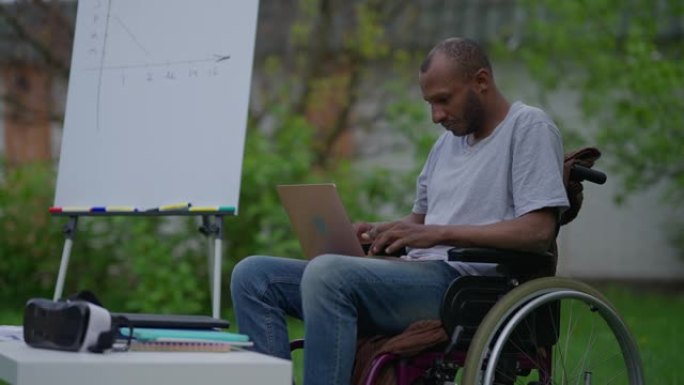 专注于轮椅上的残疾人在慢动作的笔记本电脑键盘上打字。非裔美国人认真的专业专家在远程工作的后院在线浏览