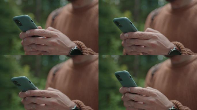 一名男子走在树林里，用手机写了一条信息。背着背包的游客在远足时在手机中打印一条消息