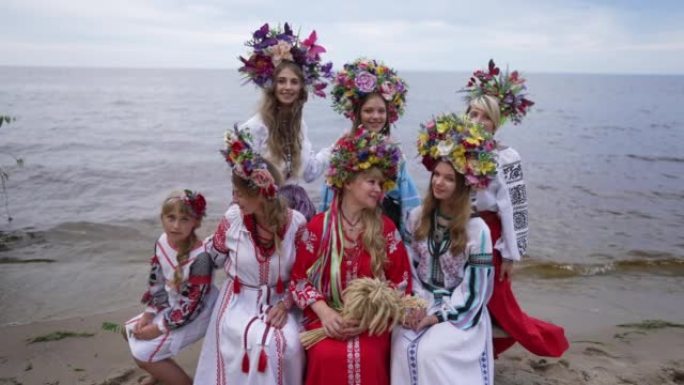 一群乌克兰年轻妇女和女孩坐在沙滩上微笑着环顾四周。穿着花环和传统服装的迷人自信的女士在户外享受春夏。