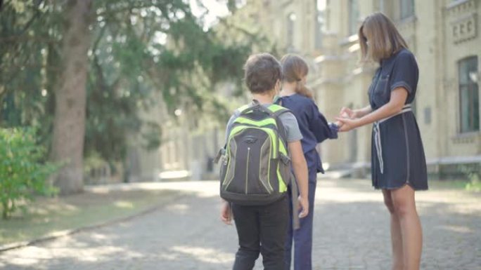 入学前，老师在中学生手上喷洒消毒剂。戴口罩的白人妇女控制新型冠状病毒肺炎消毒的学童。冠状病毒教育理念