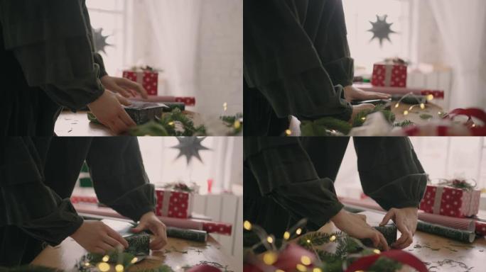 组装和准备圣诞礼物的侧视图。一个女人的特写镜头用带有圣诞节装饰品的包装纸将她的手包裹在盒子上。专业装