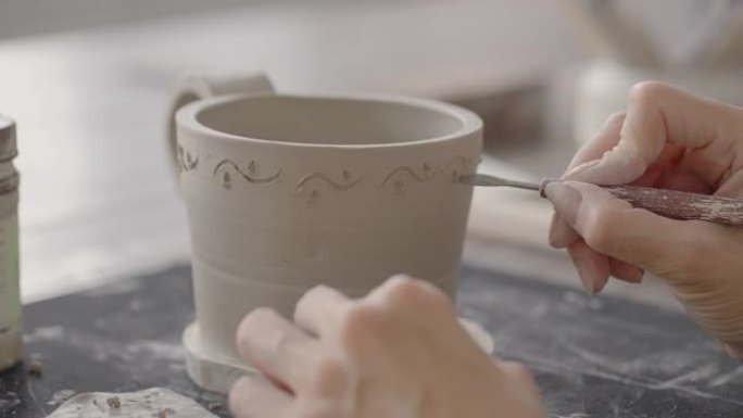 女人在陶瓷板上绘画时的手。制作手工粘土菜肴的波特车间。艺术家在陶器车间在陶器上创造了美丽的图案。特写