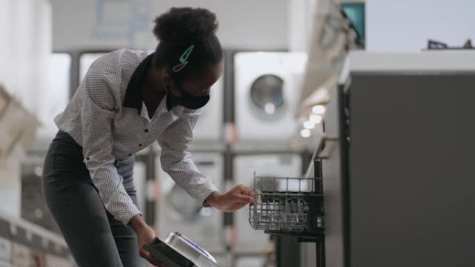 年轻的黑人女士正在家电商店中选择洗碗机，购买厨房设备