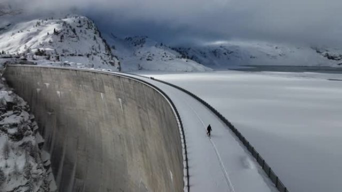 空中无人机拍摄的一名男子穿越山区积雪覆盖的大坝