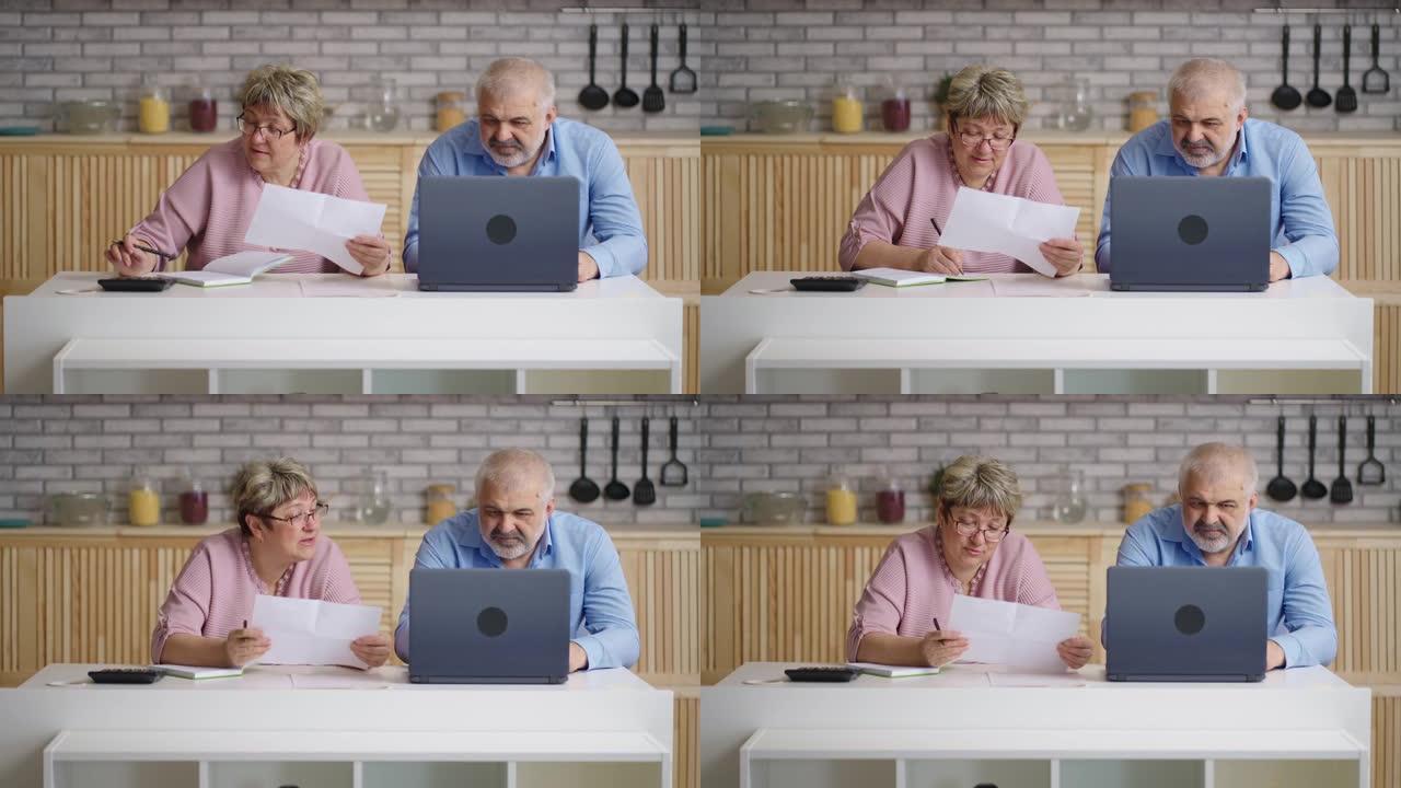 已婚的老年夫妇正在检查水电费，妻子和丈夫正在查看纸张，依靠计算器并通过笔记本电脑在线付款