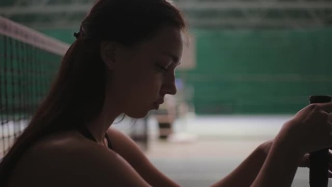 年轻的女运动员在输掉比赛后坐在网球场上的网旁，扭动球拍并思考失败，特写肖像