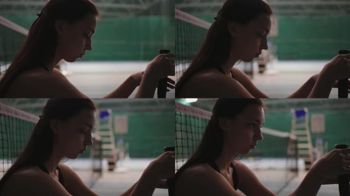 年轻的女运动员在输掉比赛后坐在网球场上的网旁，扭动球拍并思考失败，特写肖像