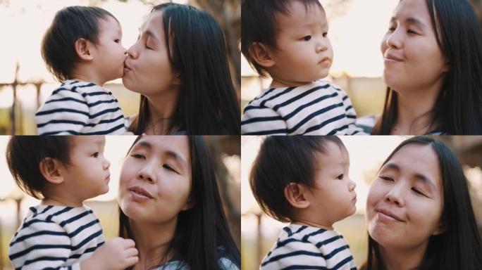 母亲在户外散步时亲吻她可爱的男孩的脸颊。