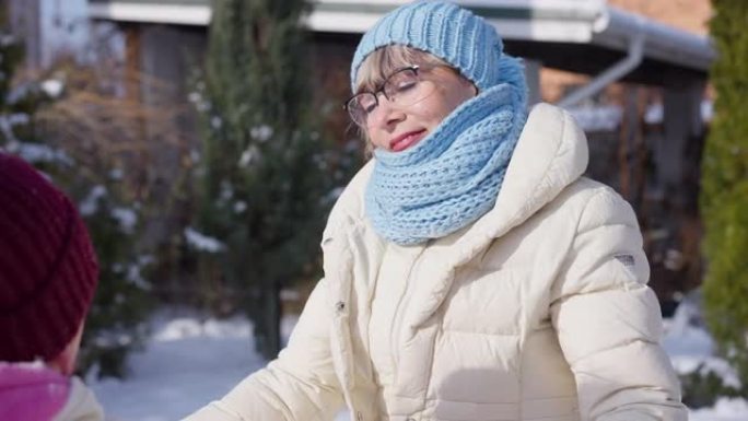 快乐的高级女人微笑的肖像在阳光明媚的冬日与女孩站在户外。可爱的高加索祖母和孙女一起享受休闲。慢动作。